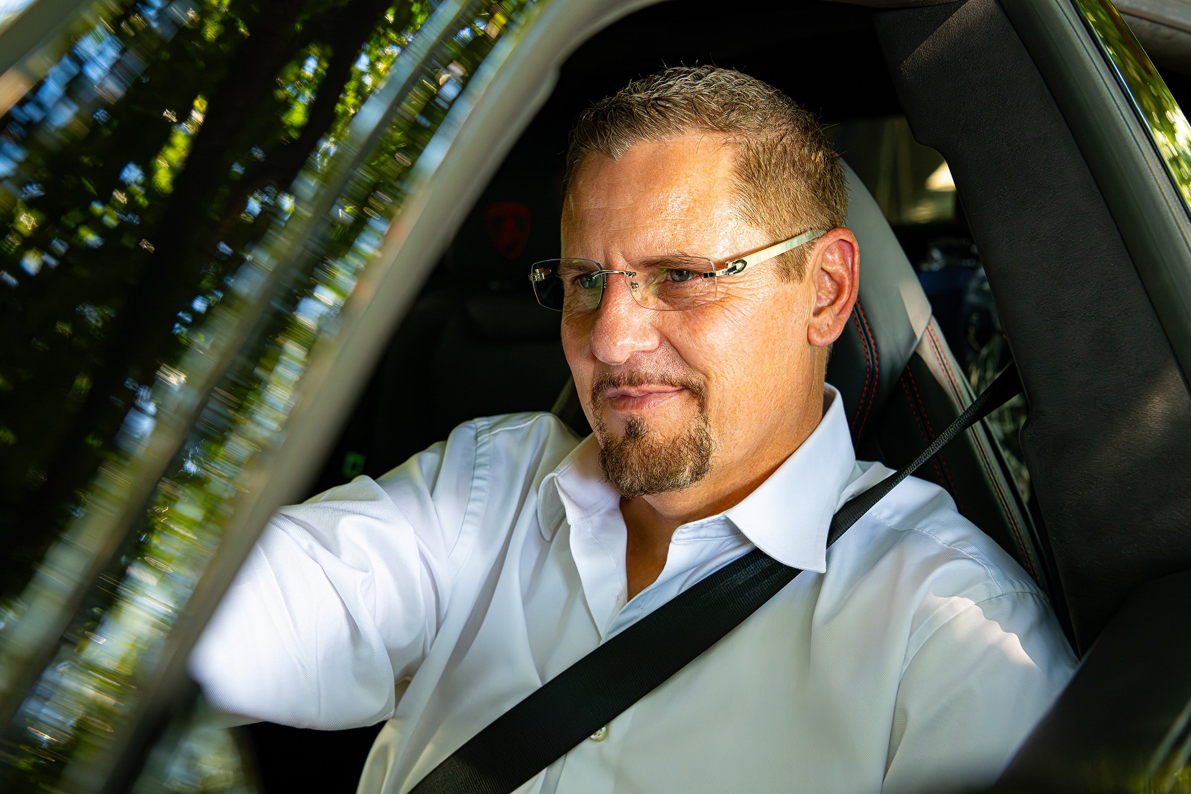 David Webb in the driver's seat of a car, wearing a white shirt